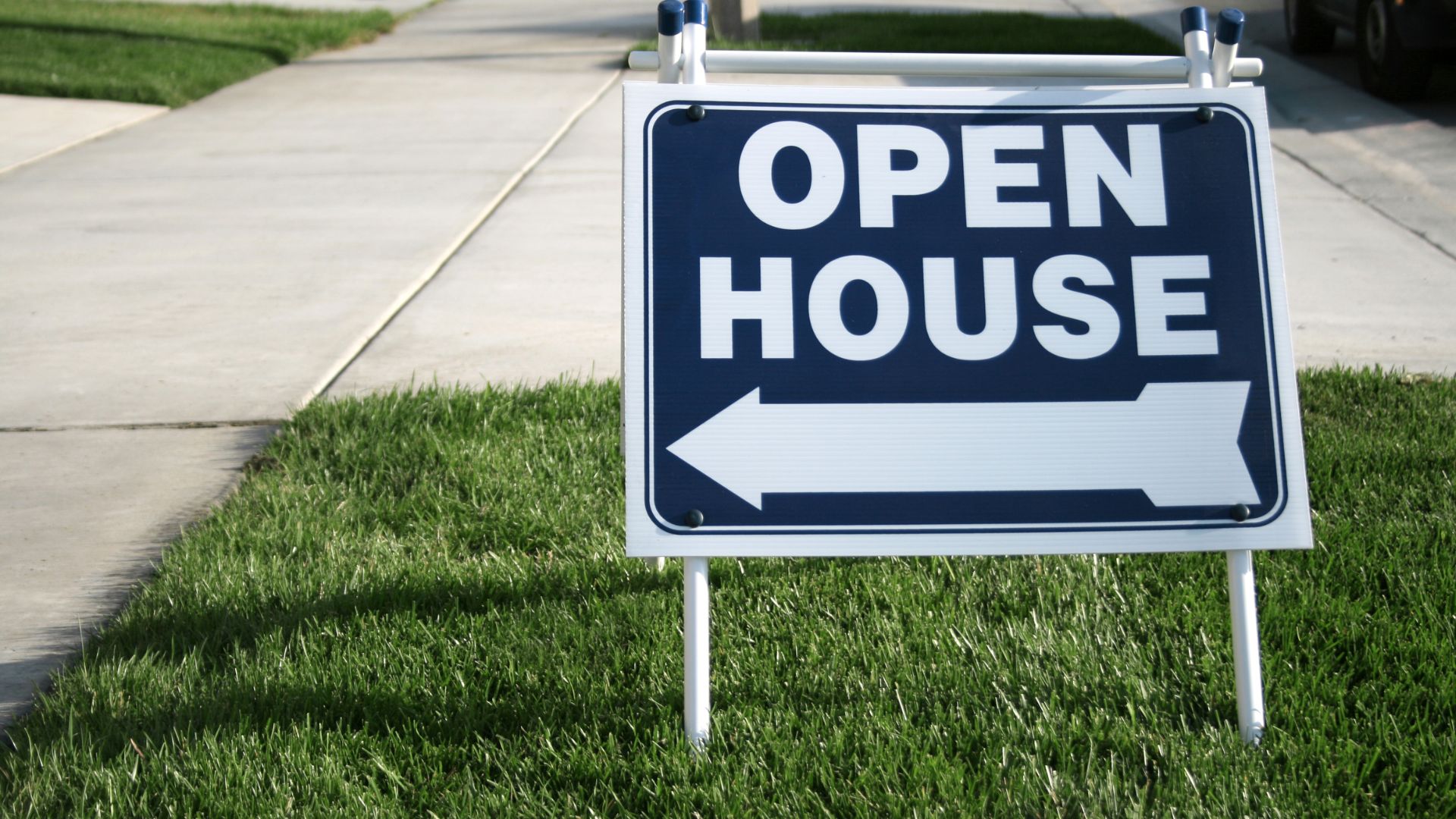 A blue and white open house sign sitting in the grass