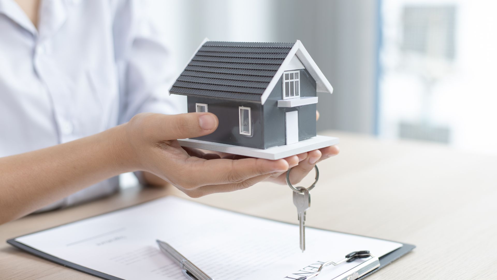 A woman holding a house model with a key in her hand